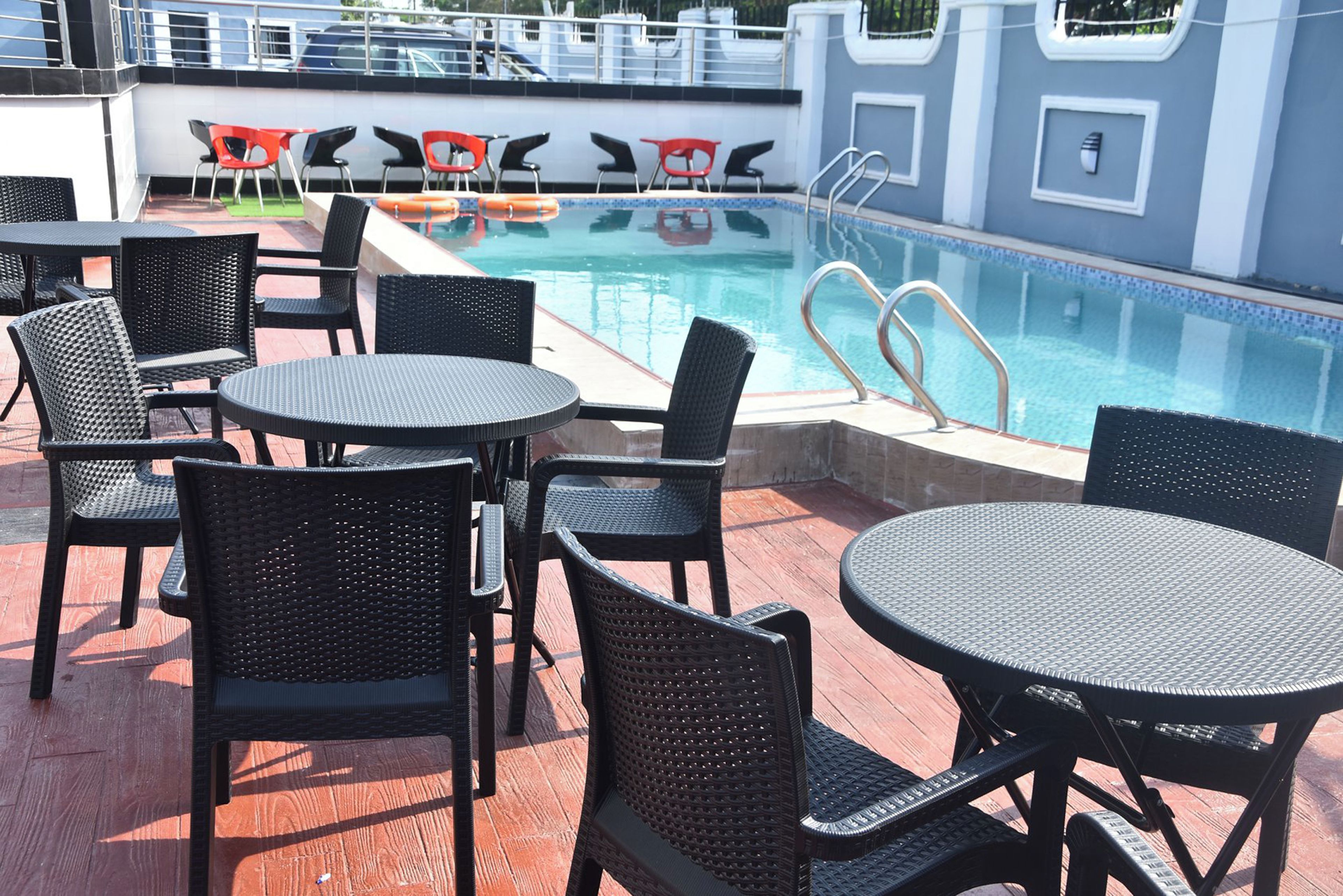 Uma área à beira da piscina com várias mesas redondas e cadeiras, uma piscina e um guarda-corpo.