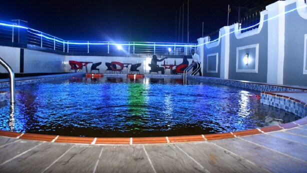 An indoor swimming pool with a tiled edge, surrounded by a white wall with a blue neon light strip. - NEW POINT HOTEL AND SUITES (Uyo)