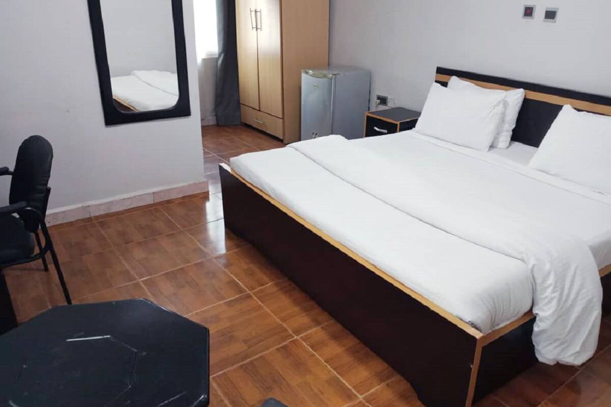 A hotel room with a bed, a desk, a chair, a wardrobe, and a mirror.