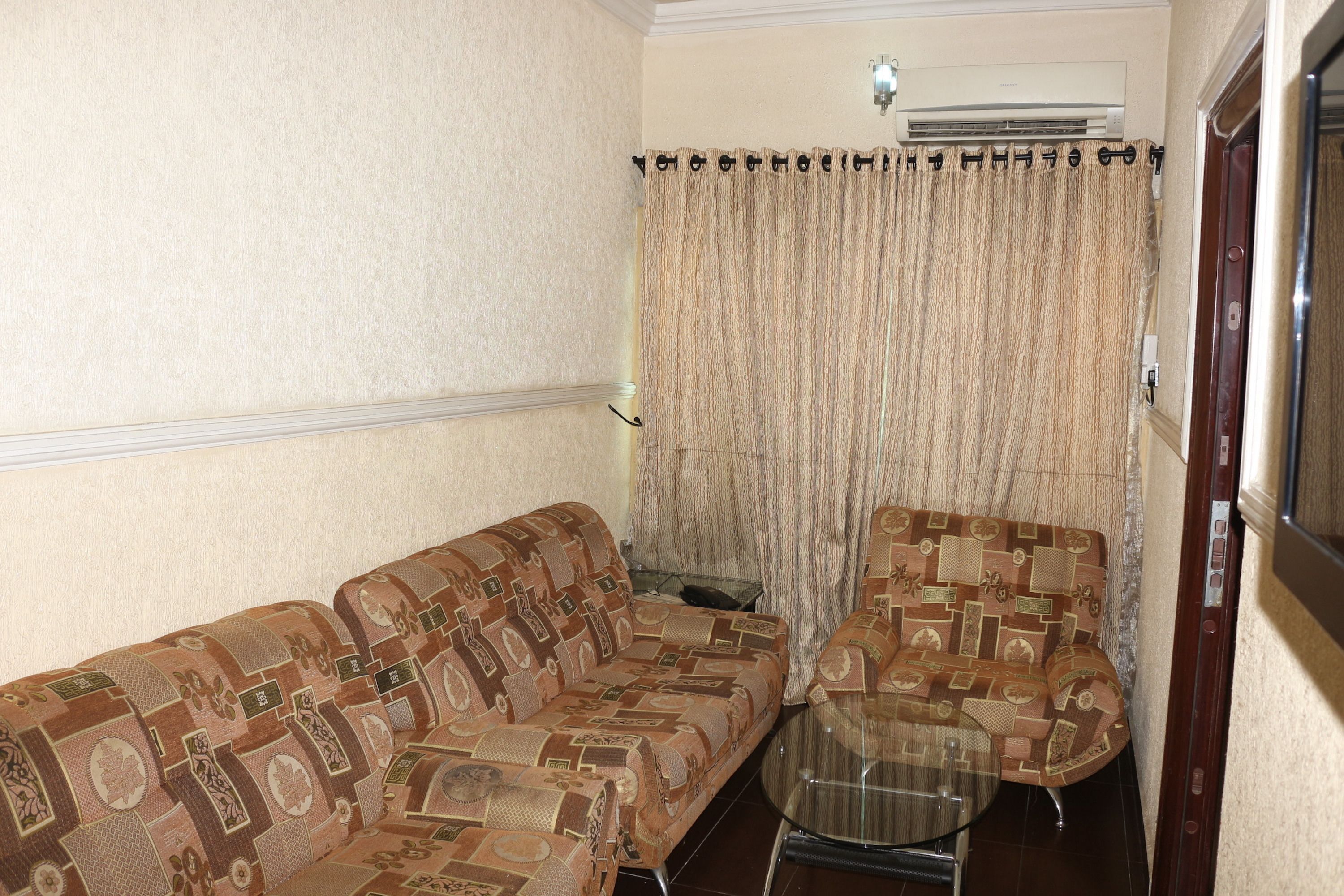 Un salon avec des canapés à motifs, une table basse en verre et un rideau.