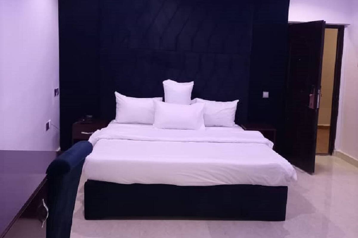 A modern bedroom with a large bed, dark headboard, and purple ambient lighting.