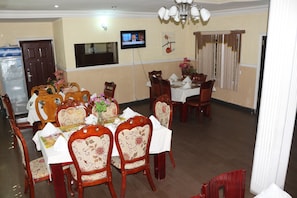 A dining area with wooden chairs and tables, a television mounted on the wall, and a water dispenser.