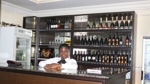 A bar area with shelves of various bottles, a refrigerator labeled "RESTAURANT", and a counter with a person seated behind it. - NEW POINT HOTEL AND SUITES (Uyo)