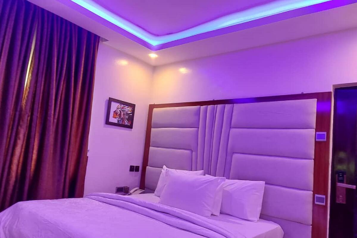 A modern bedroom with a large bed, a headboard with vertical slats, and purple ambient lighting.
