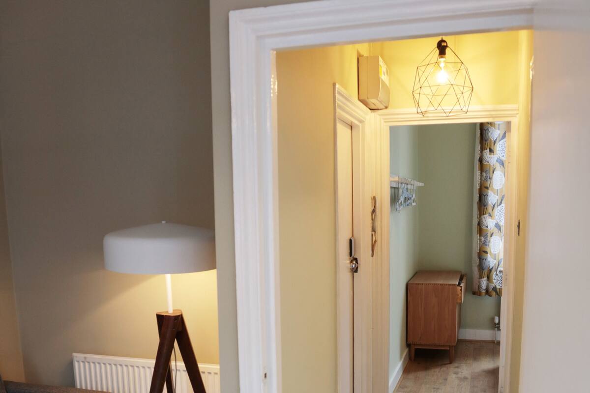 A hallway with wooden flooring, a lamp, a radiator, and a door leading to another room.