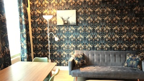 A room with a patterned wallpaper, a grey sofa with a cushion, a wooden table, and a floor lamp. - Kings Cross Apartments (London)