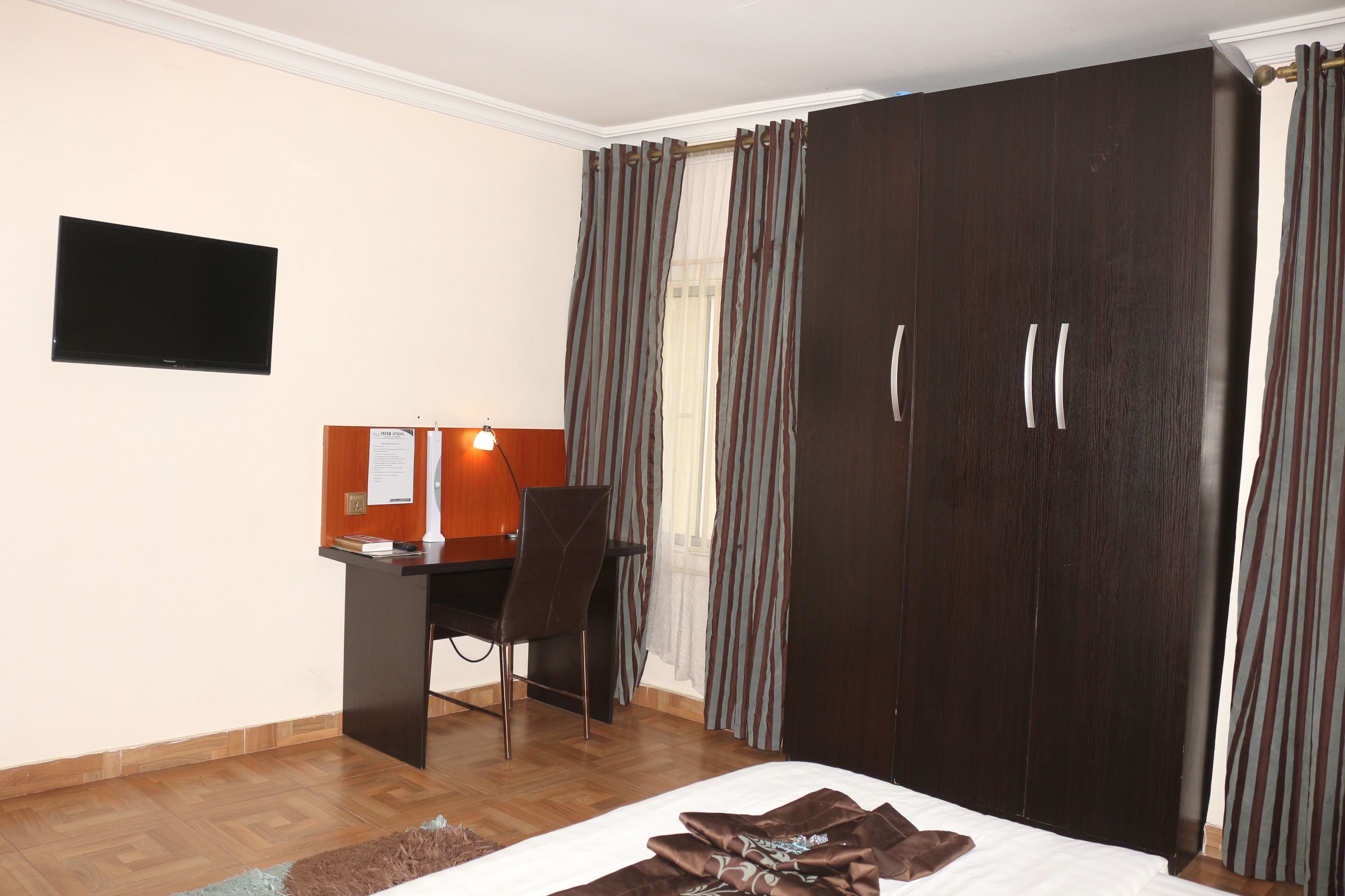 A hotel room with a bed, a desk, a chair, a TV, and a wardrobe.