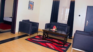 A living room with a sofa, armchairs, a coffee table, and a red and black rug. - Fresh Spring Hotels & Towers (Uyo)