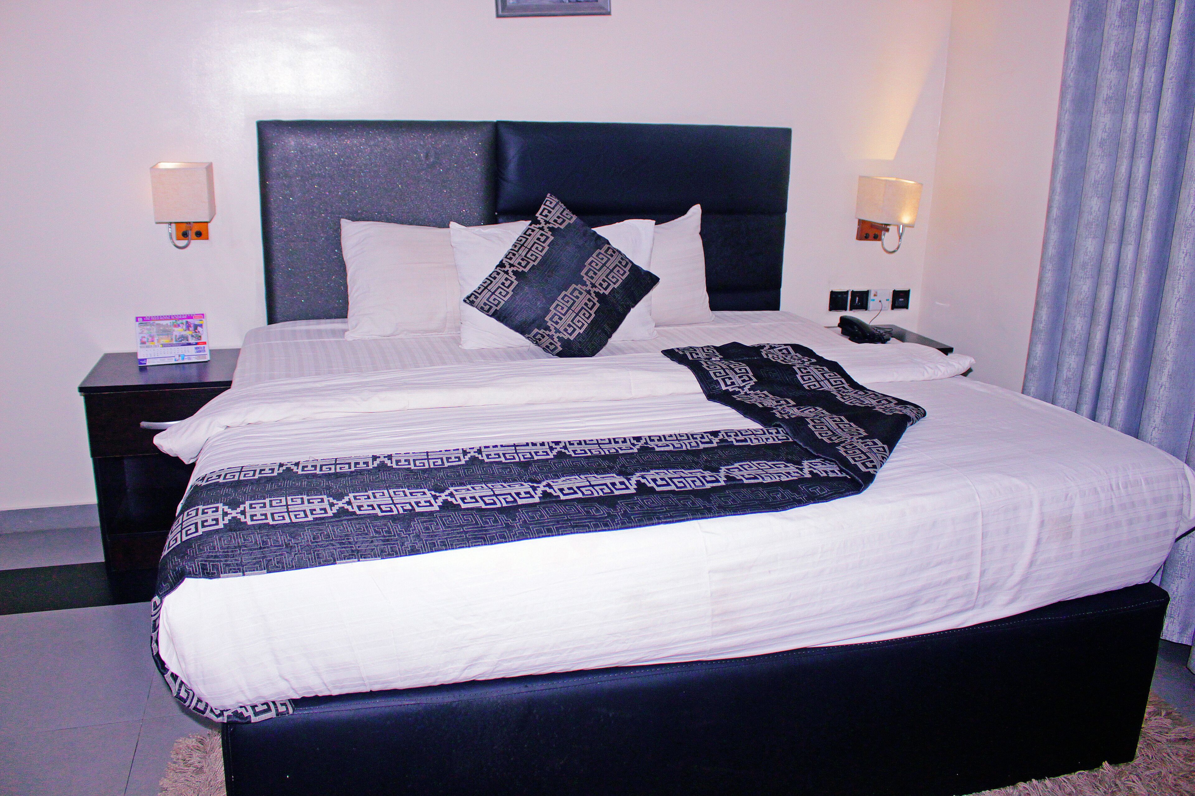 A neatly made bed with a patterned bedspread and pillows, a bedside table with a book, and wall-mounted lamps.
