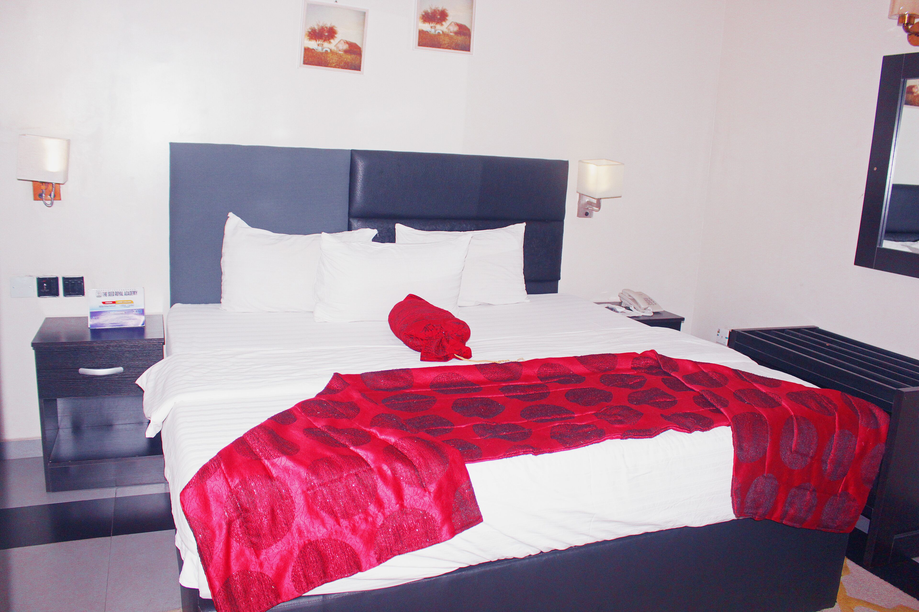 A hotel room with a large bed, a nightstand, a lamp, and a wall-mounted phone.