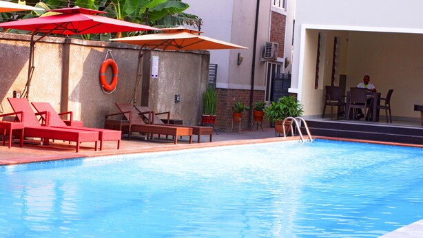 A swimming pool with red lounge chairs and umbrellas, a lifebuoy, and potted plants. - Fresh Spring Hotels & Towers (Uyo)