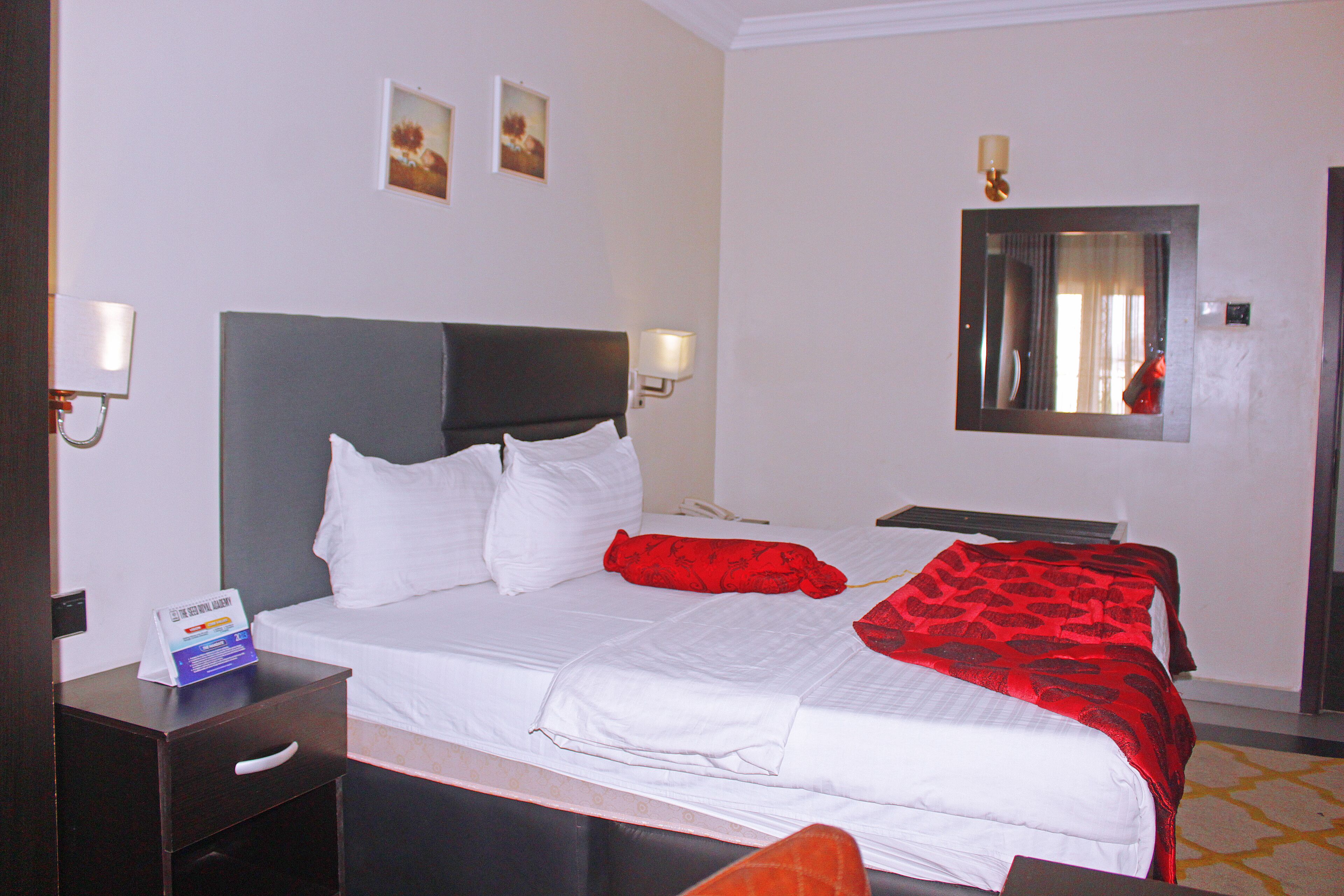 Quarto de hotel com cama, mesas de cabeceira, um espelho e luminárias na parede.