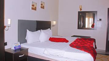 Quarto de hotel com cama, mesas de cabeceira, um espelho e luminárias na parede.