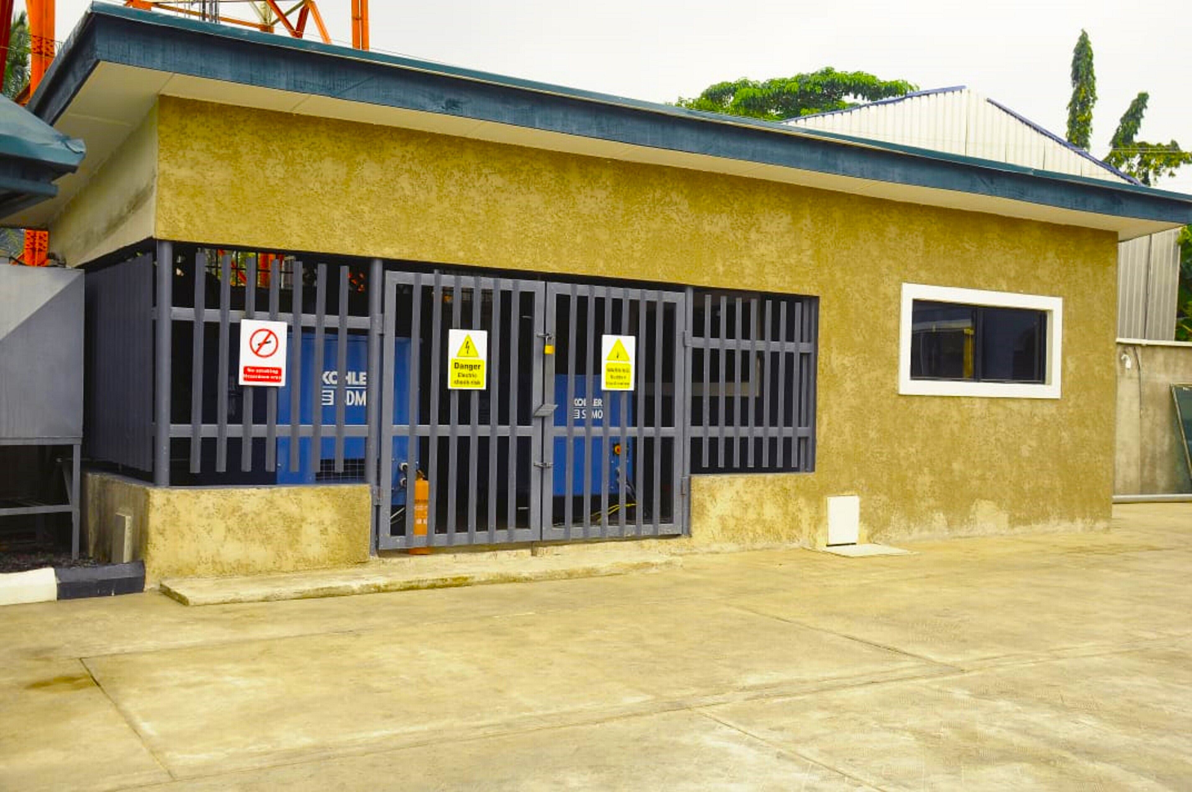 A building with a yellow exterior, a barred entrance, and warning signs.