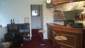 A bar area with a wooden counter, bar stools, a bookshelf with books, and a clock on the wall. - Byrdir House (Harlech)