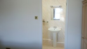 A bathroom with a pedestal sink, a mirror above it, and a light fixture on the wall. - Byrdir House (Harlech)