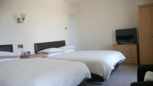 A hotel room with two single beds, a wooden dresser, a television on top, and a wall-mounted light fixture. - Byrdir House (Harlech)