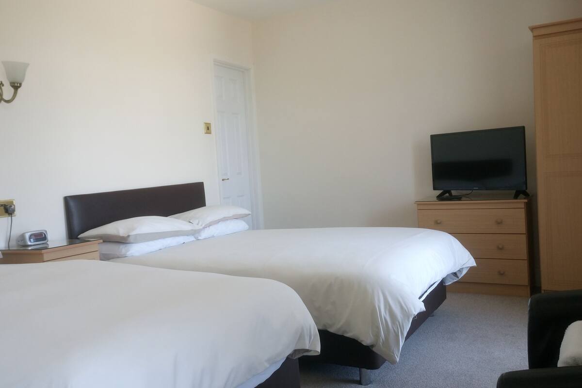 A hotel room with two single beds, a wooden dresser, a television on top, and a wall-mounted light fixture.