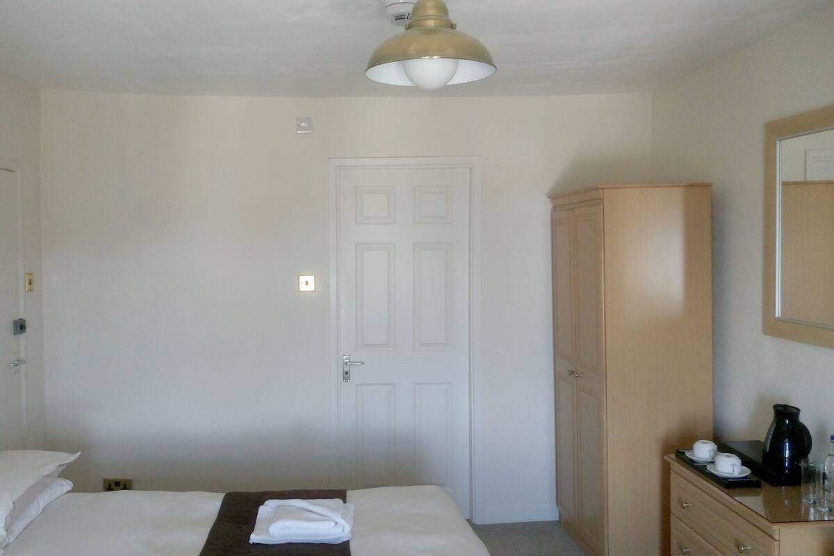 A hotel room with a bed, a wardrobe, a mirror, and a nightstand with a lamp.