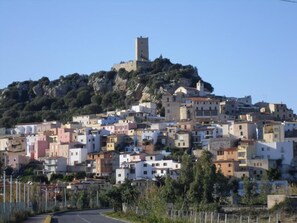 Une ville côtière avec des bâtiments construits sur une colline, une tour imposante et une route menant à la ville.
