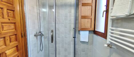 A glass-enclosed shower with a wooden door, tiled walls, and a wooden cabinet with a towel hanging on it.