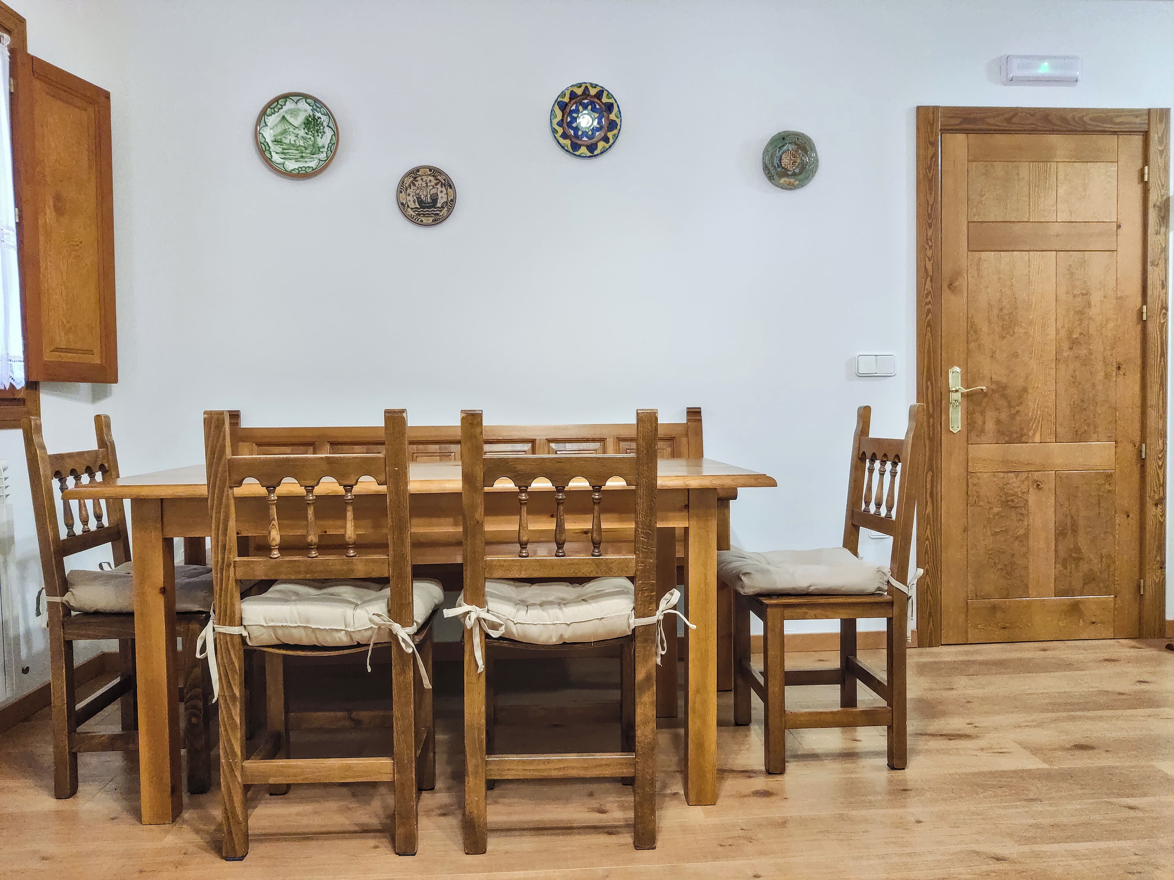 A wooden dining table with four chairs, a wooden door, and three decorative plates on the wall.