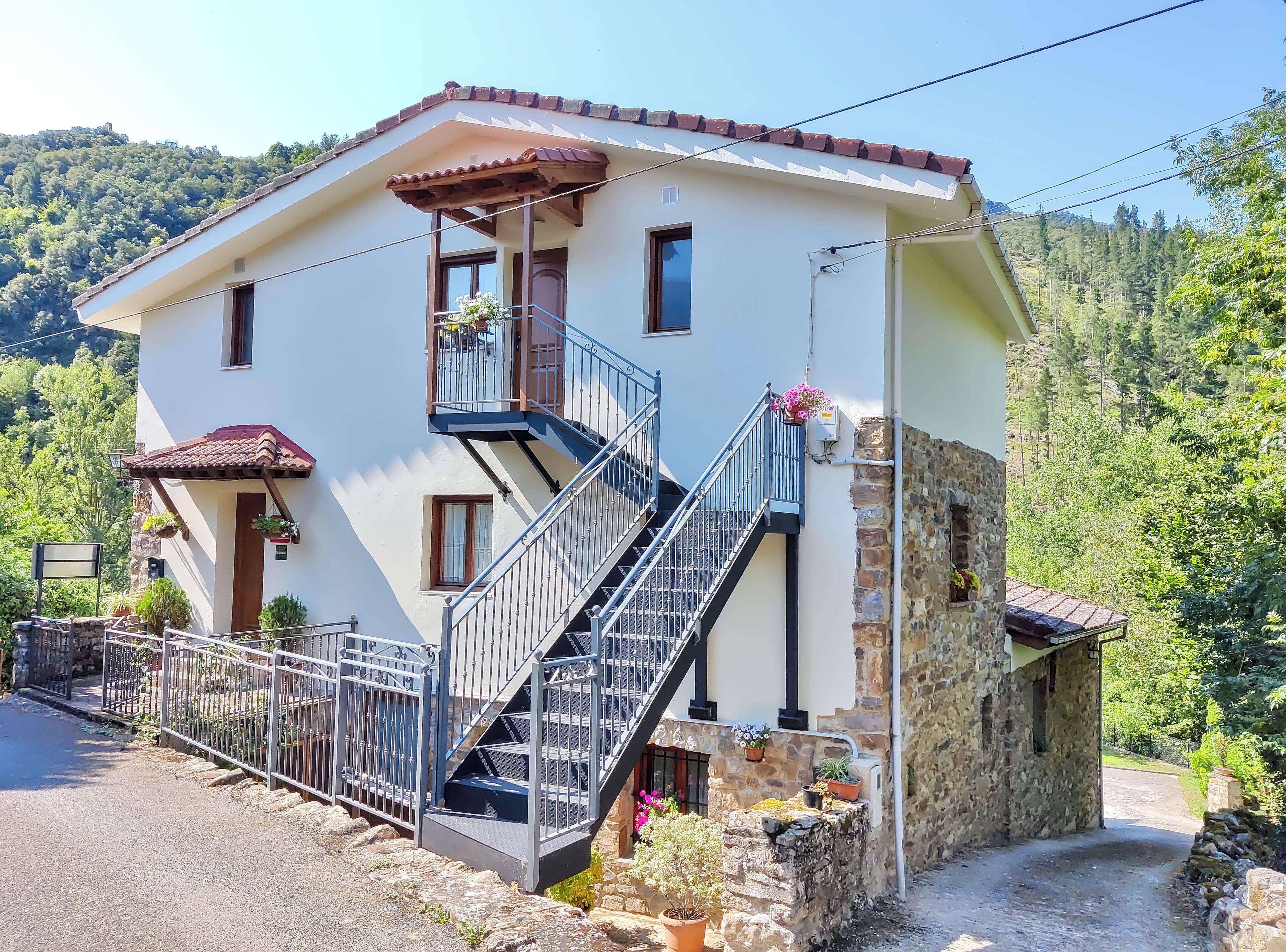 Una casa de dos pisos amb un balcó, una escala i una paret de pedra.