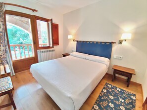 A bedroom with a large bed, two bedside tables, a window with a view, and a door leading to a balcony. - Apartamentos Javier (Camaleno)