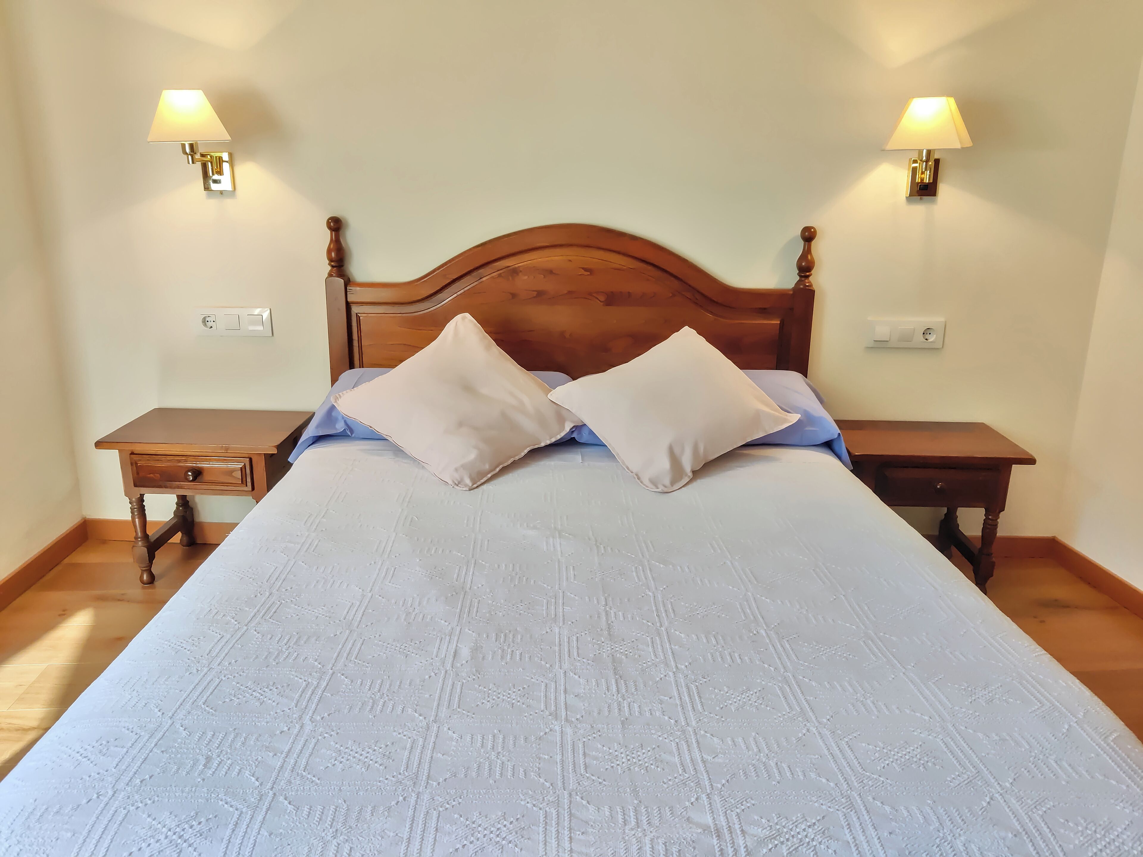 A neatly made bed with a wooden headboard, two bedside tables, and wall-mounted lamps.