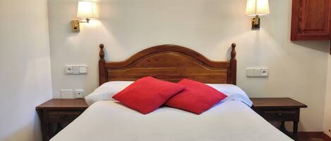 Una cama bien hecha con cabecera de madera, dos mesitas de noche y dos lámparas de pared.
