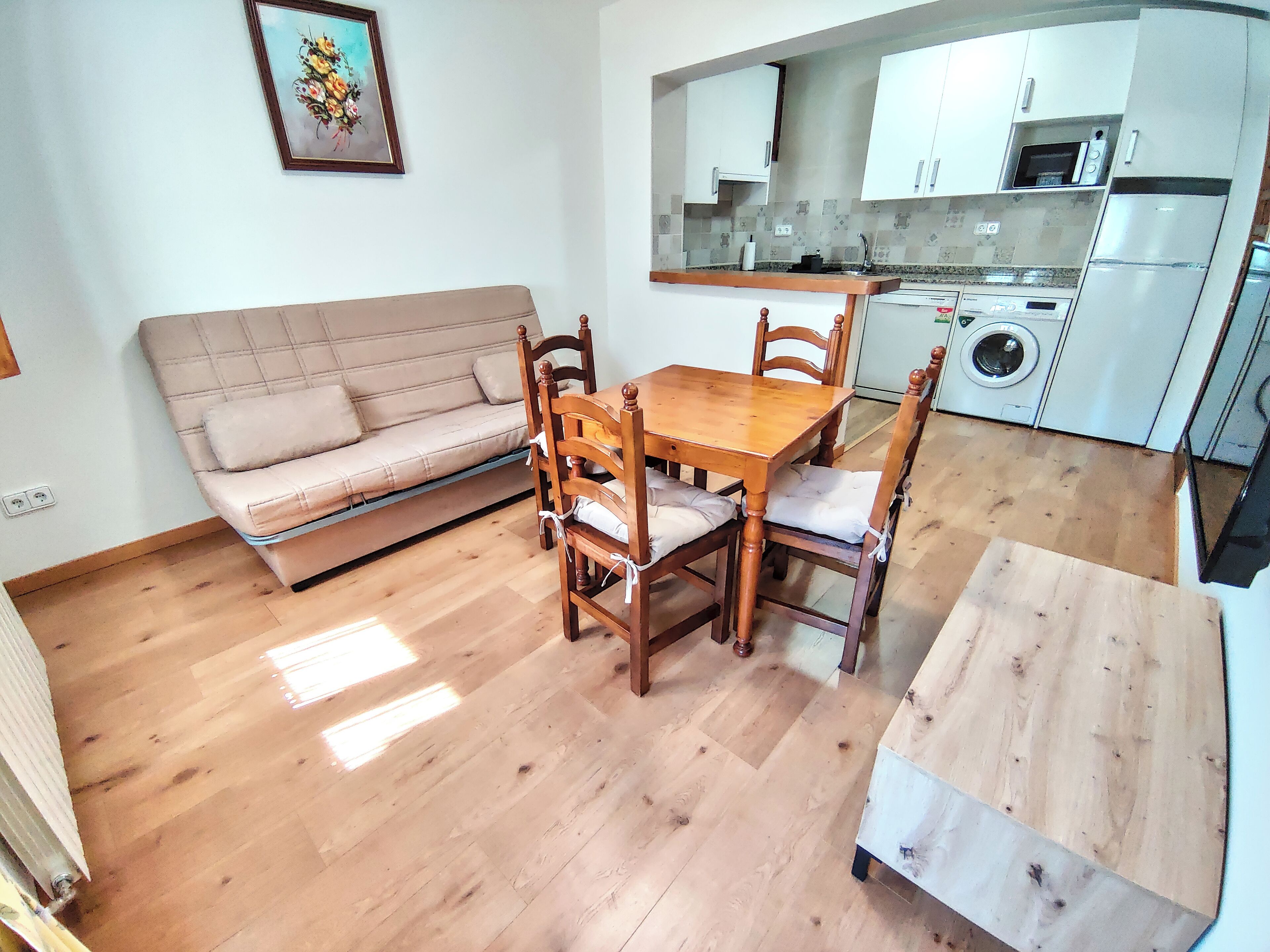 Un espacio habitable compacto con sofá, mesa de comedor de madera, sillas, una pequeña cocina equipada con microondas y lavadora.