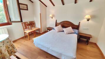 A bedroom with a large bed, wooden headboard, two bedside tables with lamps, a wooden bench, a chair, and a window with curtains.