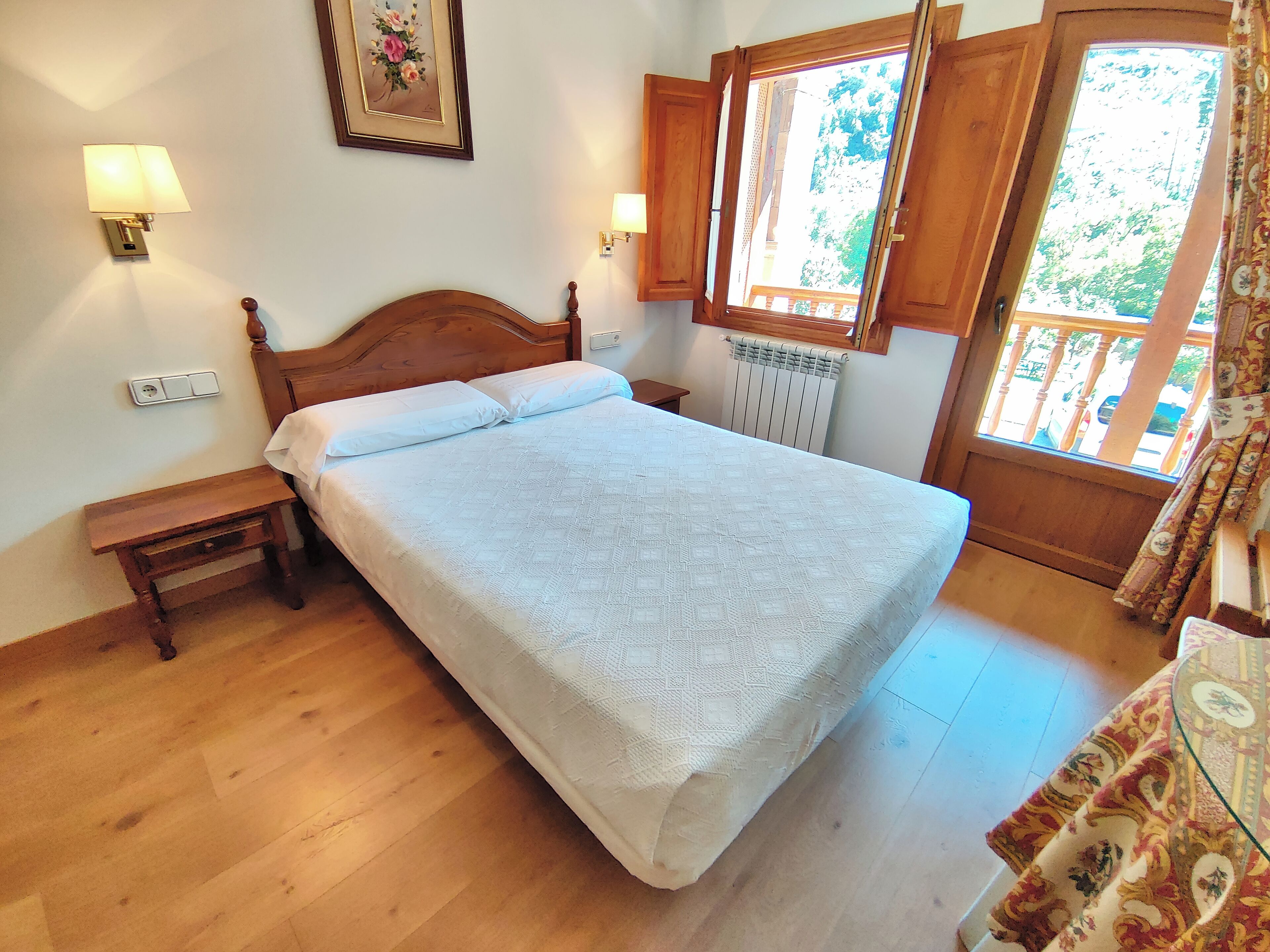 Une chambre à coucher avec un lit en bois, deux tables de chevet, un radiateur et une fenêtre avec des rideaux.
