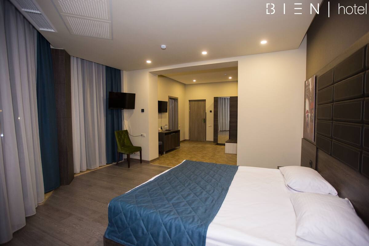 A hotel room with a large bed, a desk, a chair, and a television.