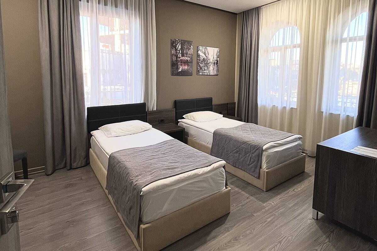 A hotel room with two beds, a desk, and a view of the city through large windows.