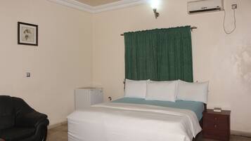 A bedroom with a bed, a nightstand, a small table, a chair, and an air conditioning unit.