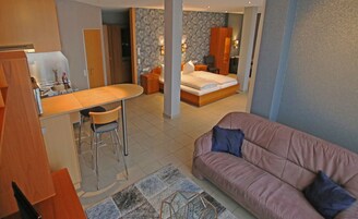 Un espacio habitable compacto con kitchenette, cama, sofá y zona de comedor.