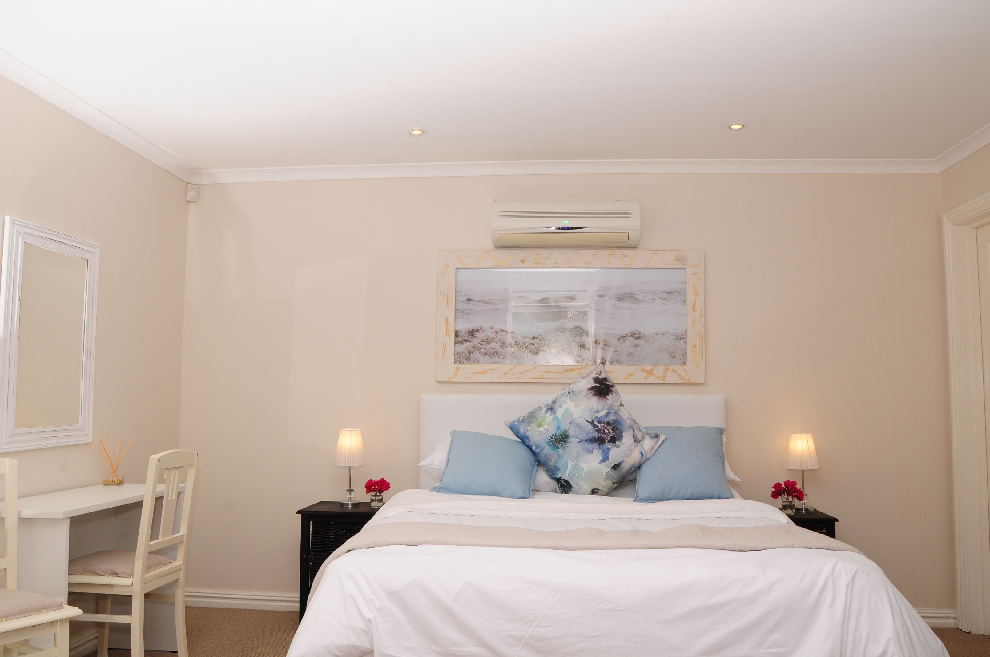 Une chambre à coucher avec un lit, un bureau et une chaise. Un climatiseur fixé au mur se trouve au-dessus du lit.