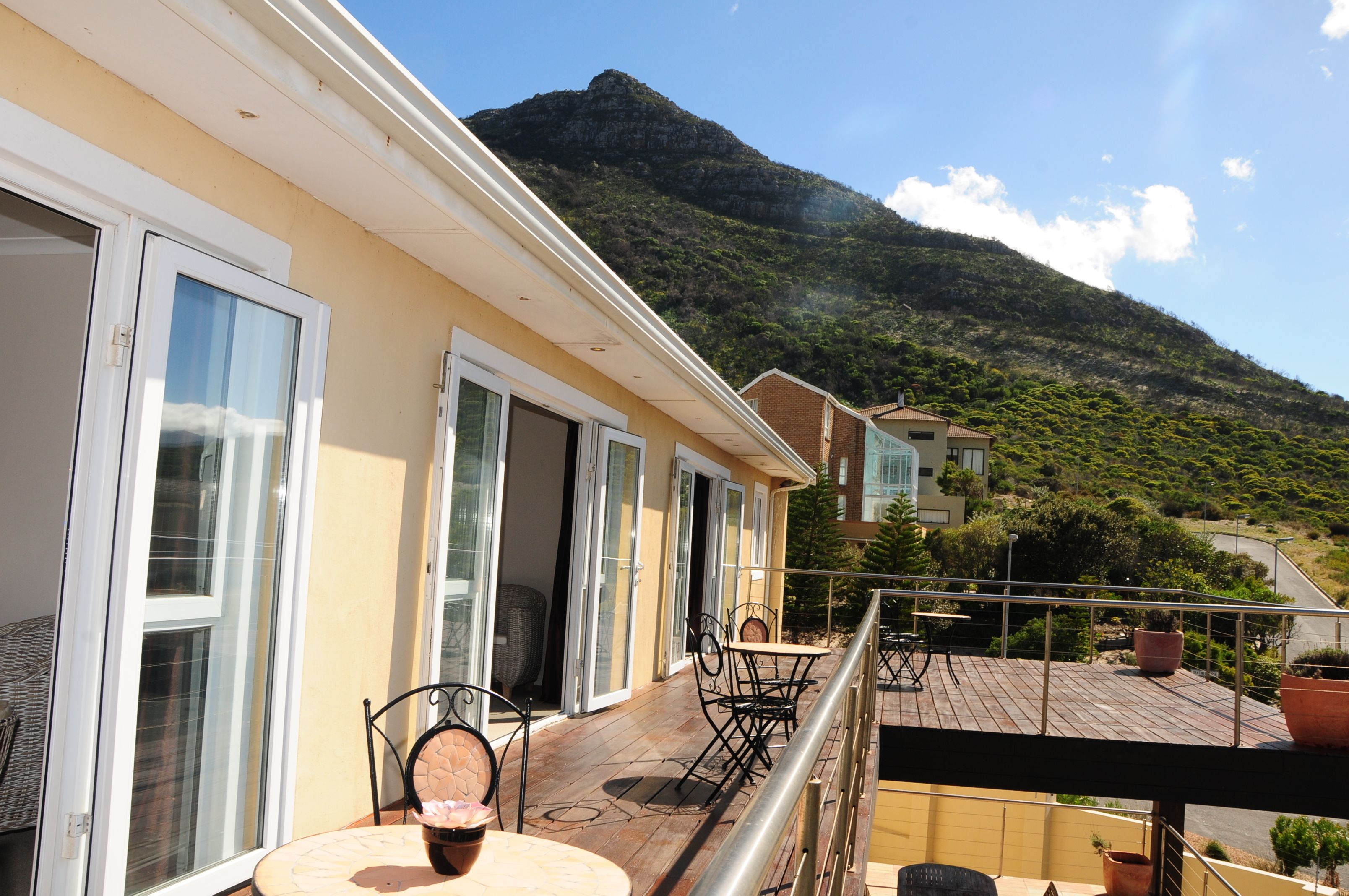 A balcony with a table and chairs, overlooking a mountain and a road.