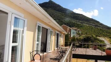 A balcony with a table and chairs, overlooking a mountain and a road.