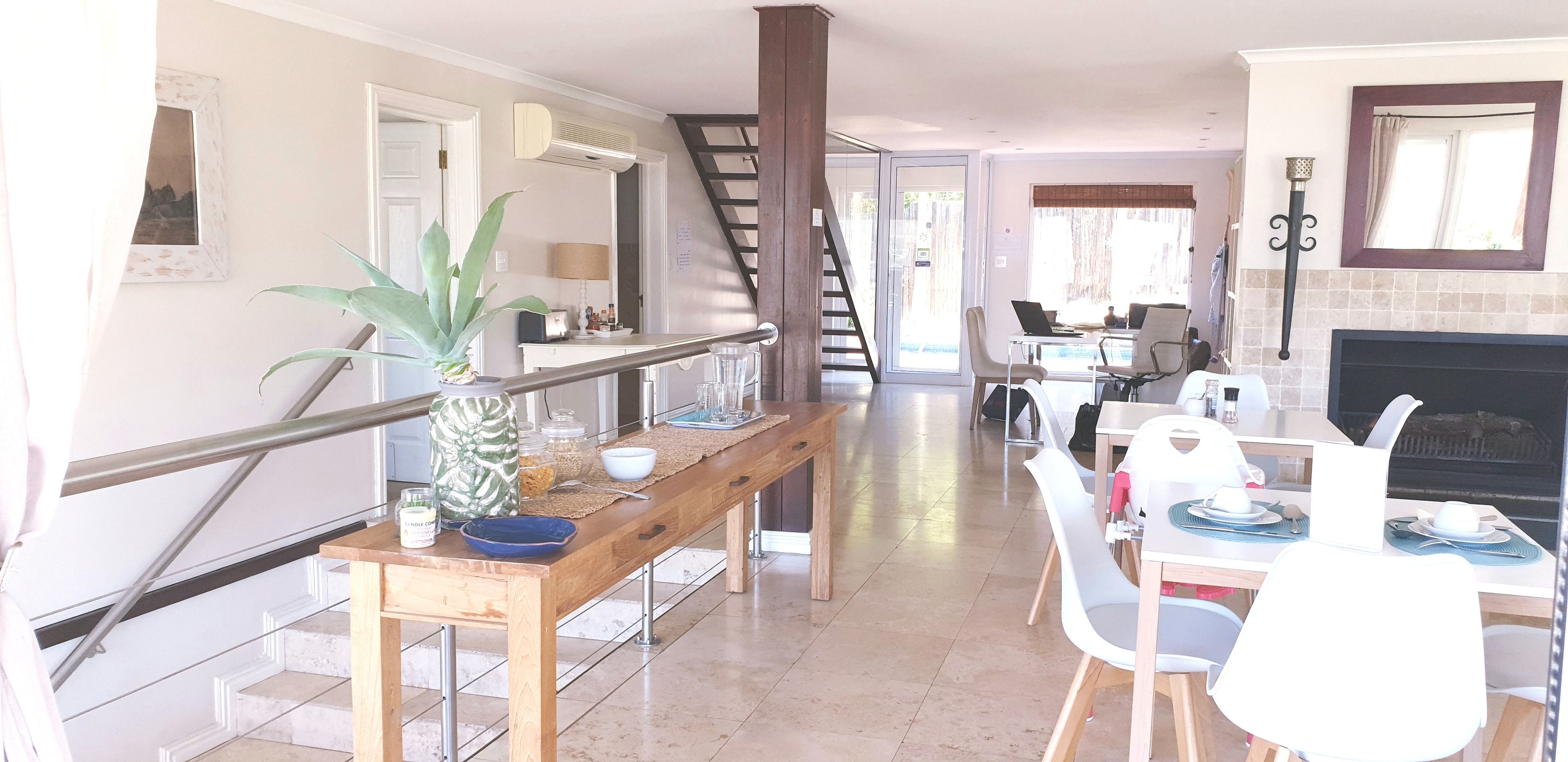 Un comedor amplio con una larga mesa de madera, sillas blancas y una escalera que lleva a otro nivel.