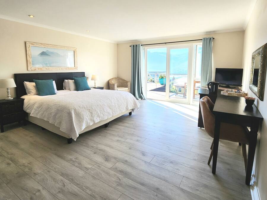 Habitación de hotel con una cama grande, un escritorio con televisor, una silla y vista al mar desde el balcón.