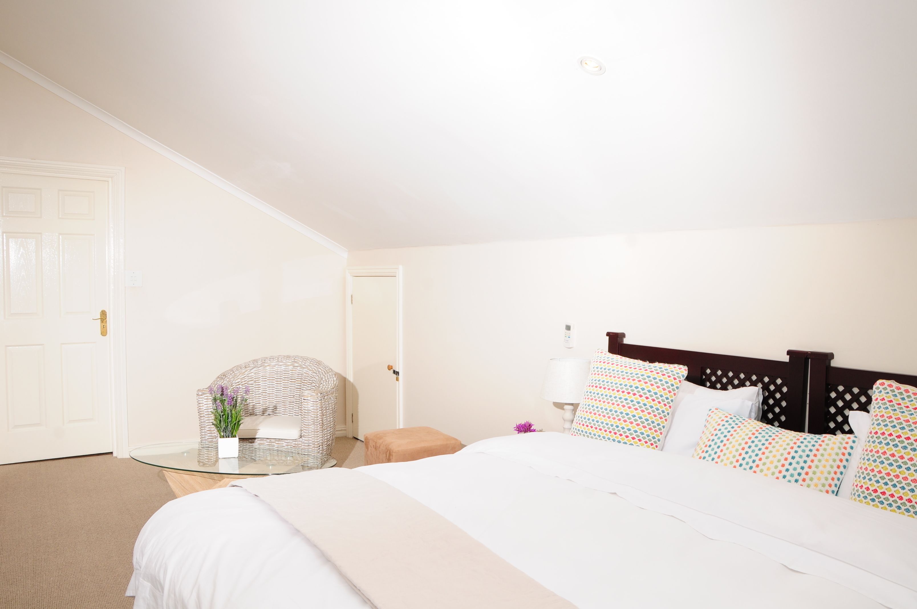 A hotel room with a bed, a glass table, a chair, and a door.