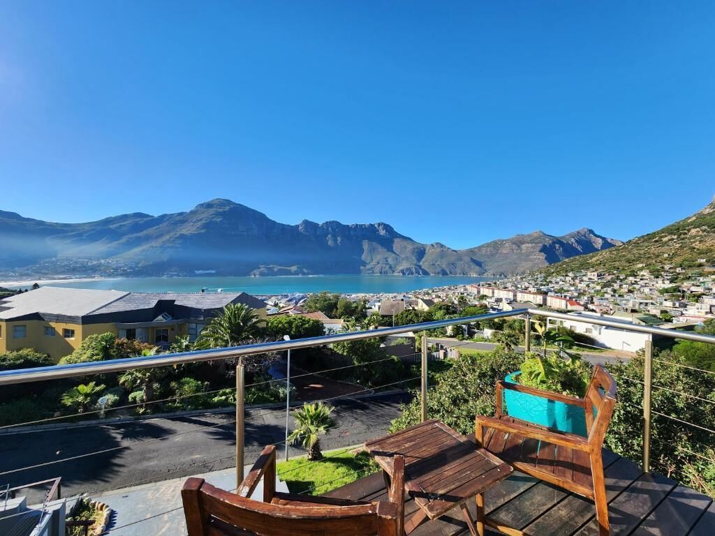 Een balkon met een houten bankje en tafel, met uitzicht op een kustplaatsje en bergen.