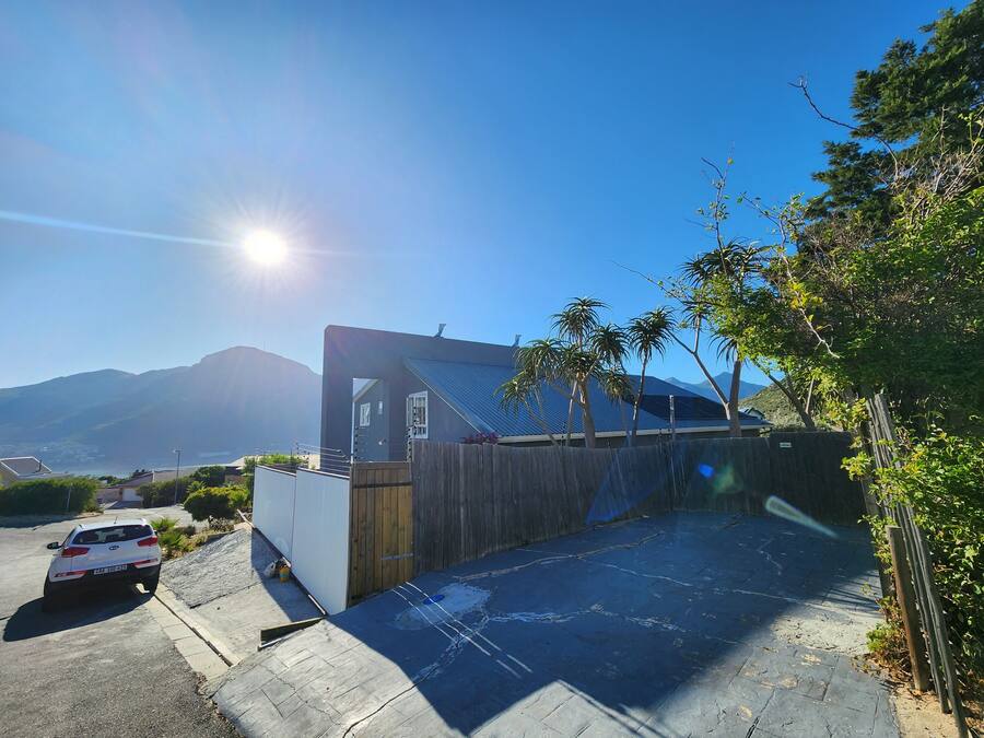 A modern building with a sloped roof, a parking area, and a view of mountains in the background.