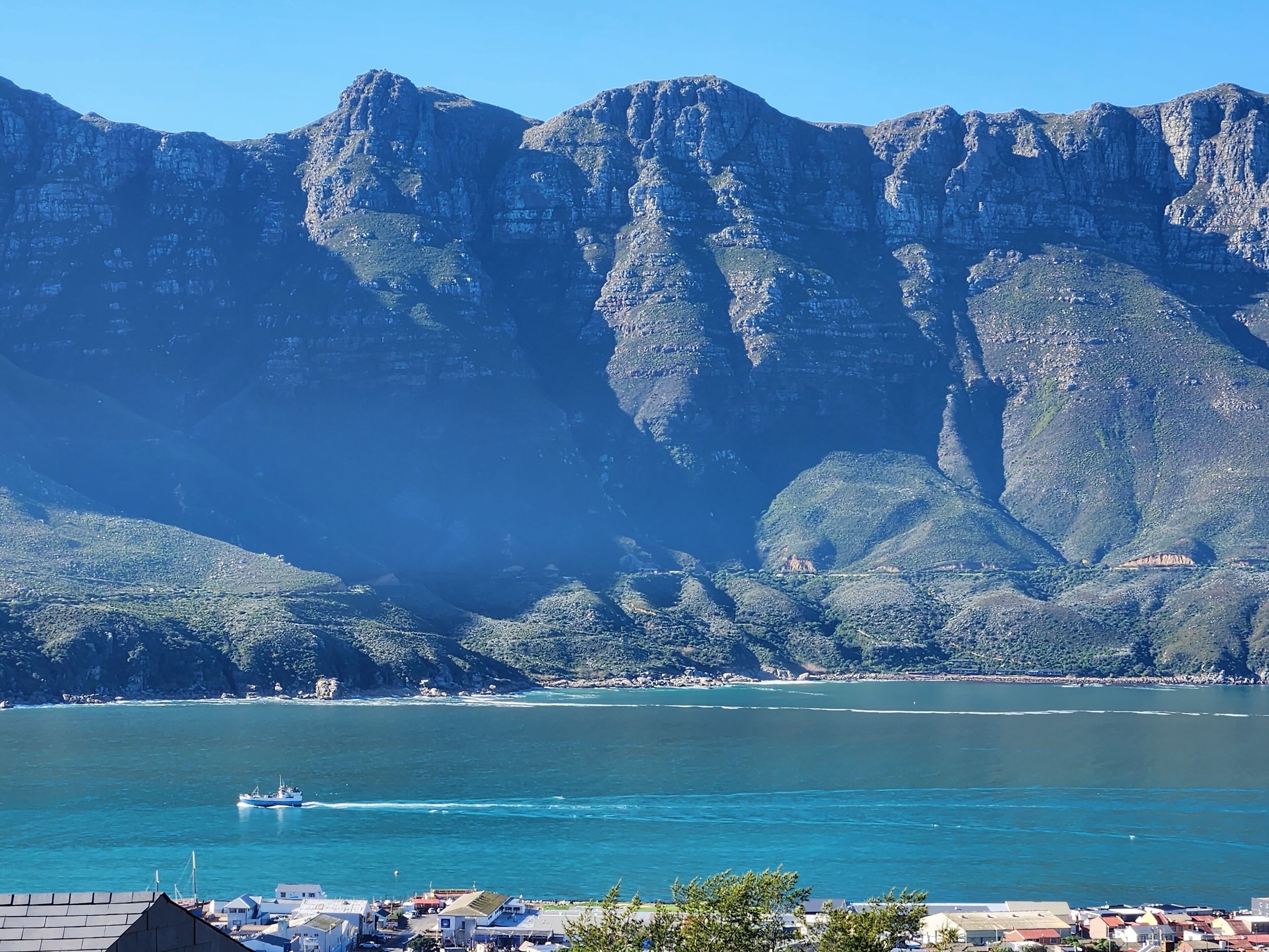 A coastal town with a mountain backdrop, a boat on the water, and buildings along the shore.