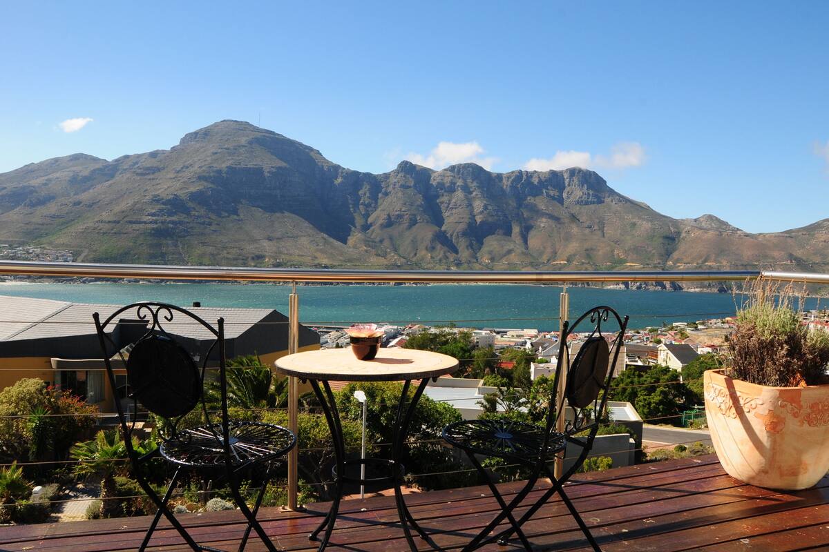 Eine Terrasse mit Tisch und Stühlen mit Blick auf eine Küstenstadt und Berge.