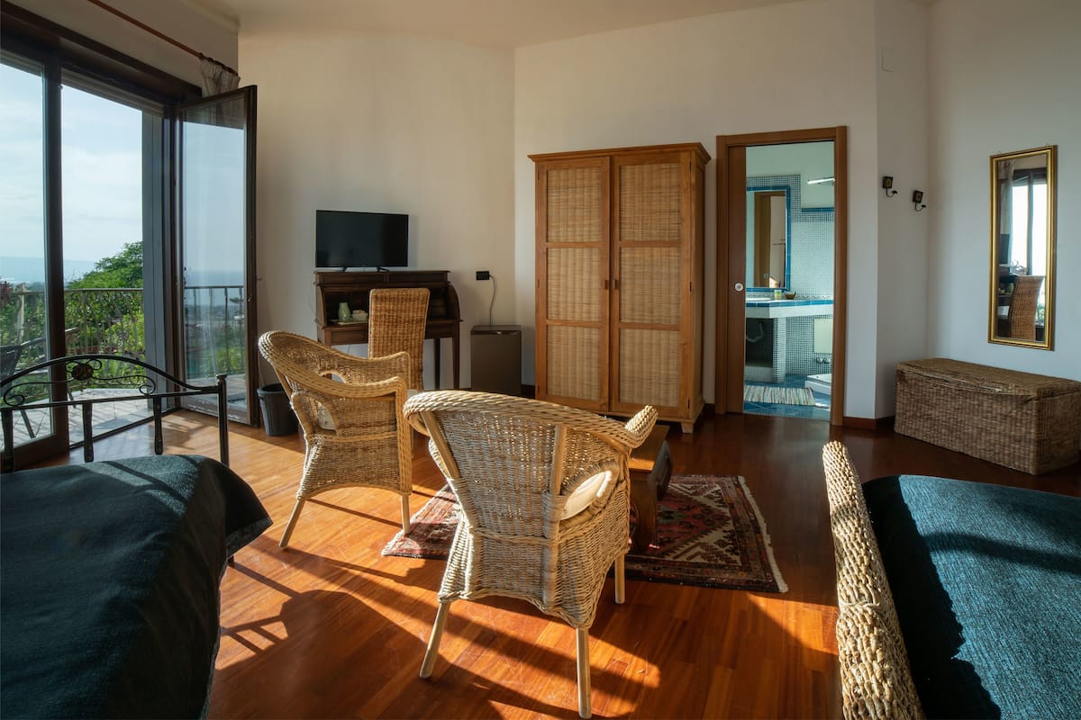 Ein geräumiges Wohnzimmer mit Balkon, Korbmöbeln, einem Fernseher und Blick ins Freie.