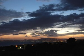 A coastal cityscape at dusk with a view of the sea and distant city lights. - Villa Patrizia BB (Ercolano)