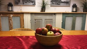 A dining table with a bowl of apples and a red table runner. There are wicker chairs, a white door, and two black lanterns on the wall. - Basement Hamburg - Hostel (Hamburg)